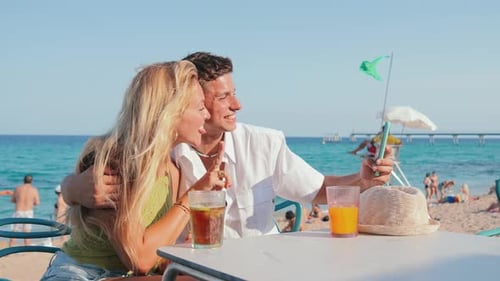 Happy Couple Enjoying a Sunny Beach Day Taking a Selfie Together at a Lively Coastal Bar