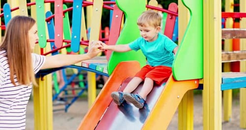 Mother and Son Playing on Playground Slide and Having Fun in the Park Outdoors