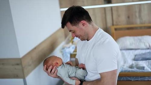 Happy new-made dad with a newborn in hands. Father waving his newborn in hospital ward.