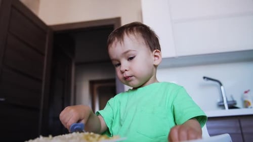 Lovely toddler eating from form. Mom helps him to pick up food from plate. Low angle view.
