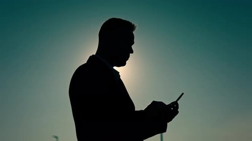 Male Silhouette Against the Background of the Sunset Sky and Sun A Man Uses a Smartphone for Work