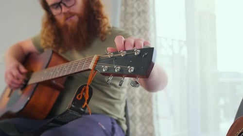 Man tuning acoustic guitar at home, close-up and medium shots