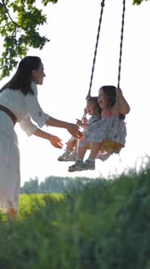 Woman Pushing Children on Swing in Countryside