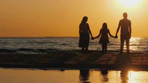 A Young Couple with a Child Stands on the Beach Watching the Beautiful Sunset