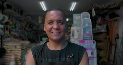 Friendly Hispanic man smiling at camera inside small hardware store, confident portrait showing