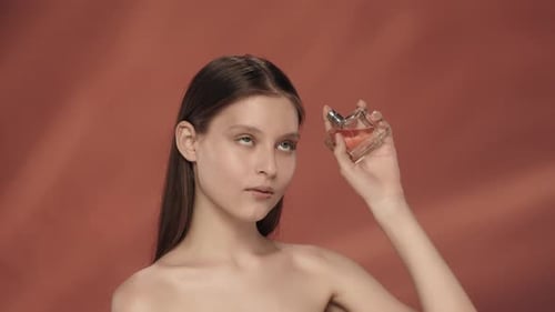 Young Woman Holding Perfume Bottle Against Orange Background