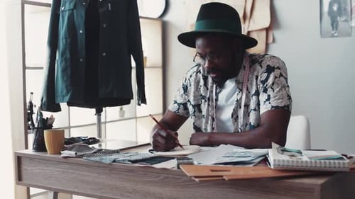 Fashion Designer Sketches Designs at Desk in Studio