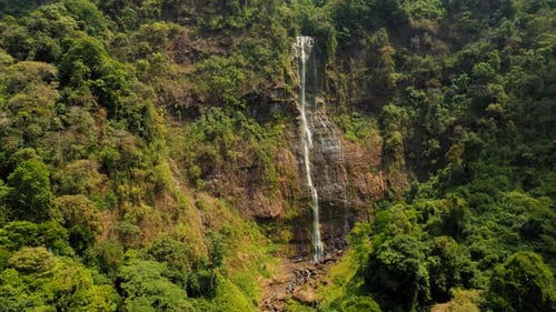 Tall waterfall cascading down rocky cliff surrounded by dense jungle in Costa Rica