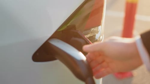 Crop of Male Hand Inserting Charging Cable Into White Electric Car at Outdoors