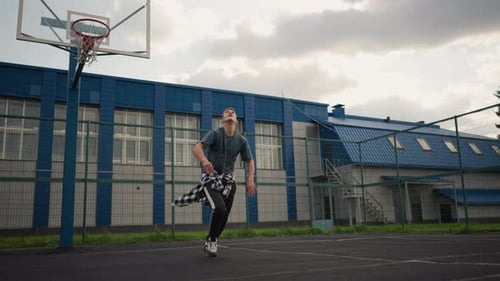 Athlete Throws Up Volleyball and Hits It on Basketball Court with Blue Building in Background