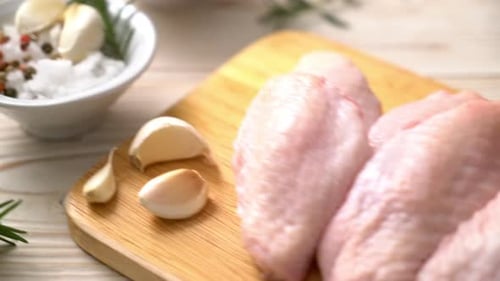 alitas de pollo frescas crudas en el medio sobre tabla de madera con ingredientes