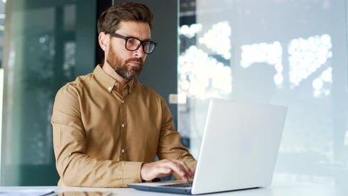 Serious thoughtful manager works on a laptop while sitting at a workplace in a business office.