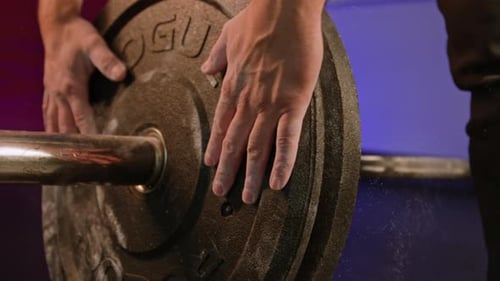 Hands Adding Weight to Barbell Rod at Gym