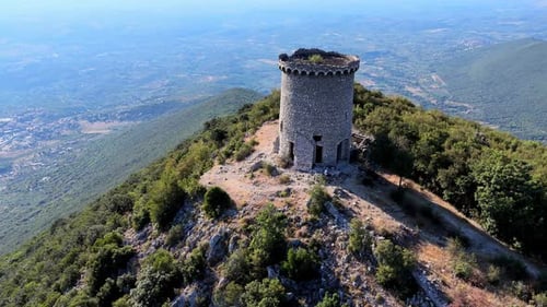 Aerial view of an ancient tower atop a hill surrounded by lush valleys and distant mountains under a