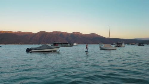 Aerial drone flying over a lake, man doing stand up paddle, with mountains at sunrise. SUP.