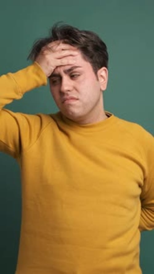 Frustrated Man Suffering From Headache in Green Studio