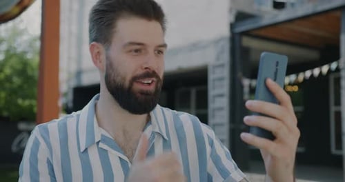 Joyful Guy Chatting on Smartphone Making Online Video Call Talking and Laughing Outdoors in City