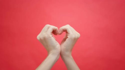 Hands Making Heart Shape on Red Background