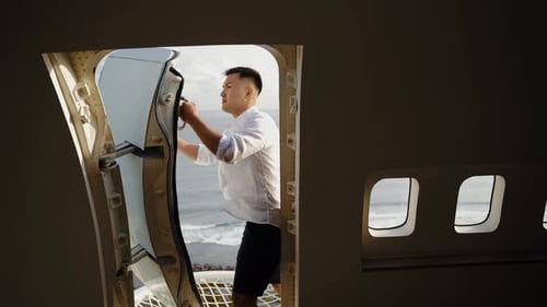 Asian man opens the door of a repurposed airplane aircraft hotel in Bali with ocean sea view.