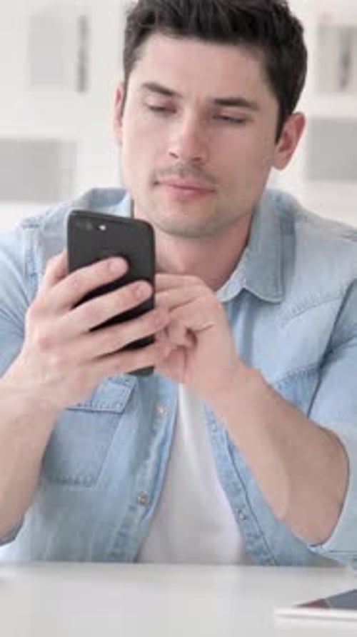 Young Adult Using Cellphone at Desk Indoors