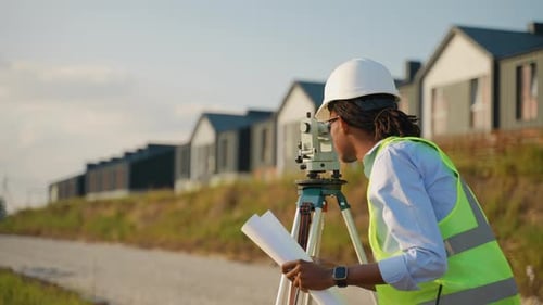 Surveyor Using Theodolite and Blueprints on Construction Site