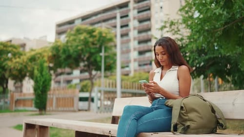 Woman Using Smartphone on Bench in Urban Park