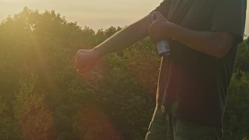 Man Uses Mosquito Spray on Mountain at Sunset