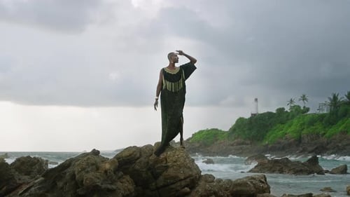 Gay Bipoc Man in Luxury Dress Boutique Brass Jewelry Makeup Poses Gracefully Tropical Rocky Hill Top