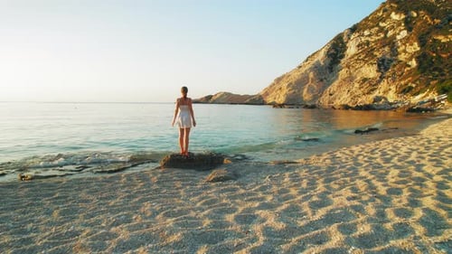 Woman standing on rocky shore at sunset on Petani Beach, Kefalonia Island Greece