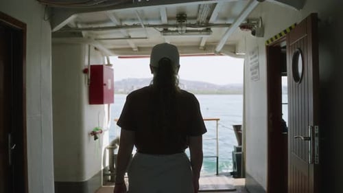 Young Woman Wearing Cap Stands on Ferry Deck Curly Haired Female Observes Ocean Skyline Travels By