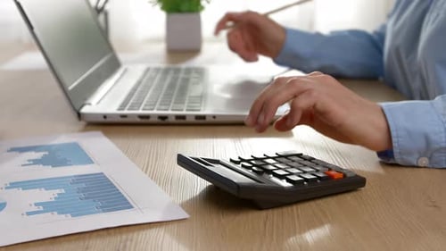 Die Hand eines Finanzmanagers zählt auf einen Taschenrechner mit einem Laptop.