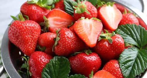 Fresh ripe strawberries in metal colander spinning on table, closeup