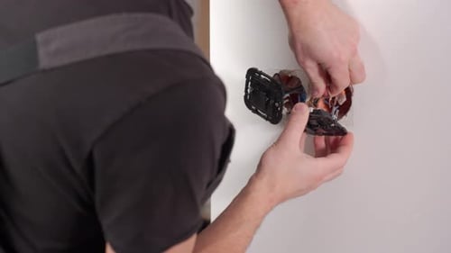 Man Connecting Electrical Wires Into Wall Socket Indoors