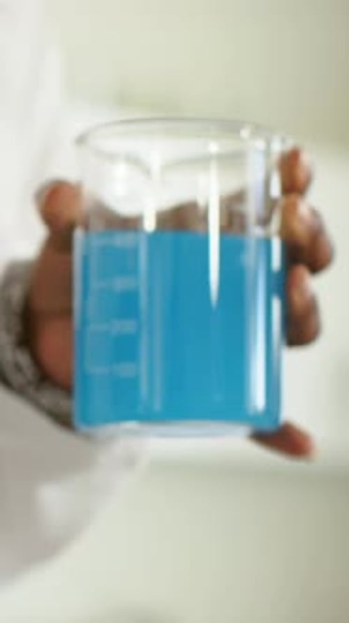 Vidéo verticale : démonstration d'une technologie de laboratoire stabilisant un bécher gradué, montrant un liquide bleu et une couche blanche