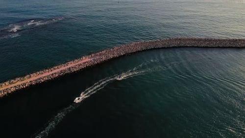Boats navigating a rocky jetty at sunset near a calm ocean