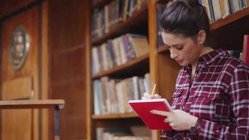 Concentrated young woman writing in library completing university assignment