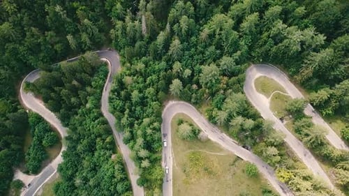 Bird's eye view with an elevating movement of a winding road inside a forest and cars passing by. 4k