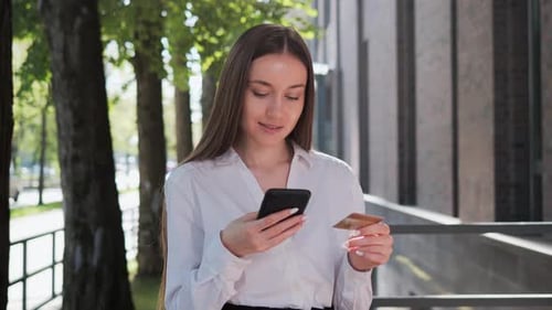 Woman Using Phone and Credit Card Outside