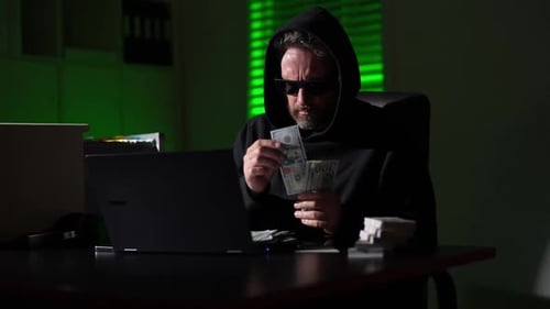Hacker Counts Dollar Bills Criminal Man in Hoodie and Glasses Counting Money in Night Office Hacker