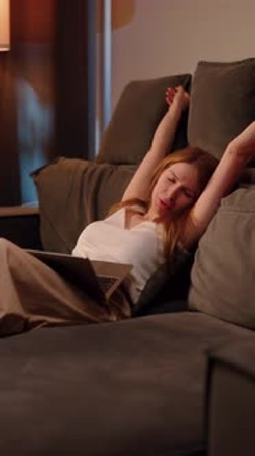 Tired Woman Lying on Sofa Reading Tablet at Home in Evening