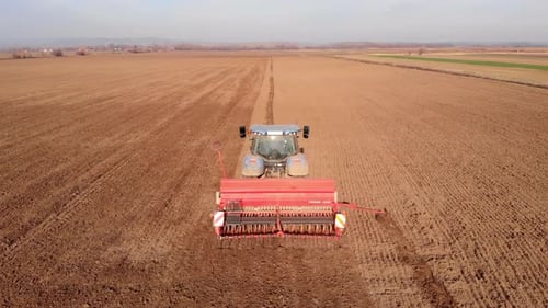 Tractor working in agricultural field, cultivating and ploughing dry soil, aerial view.