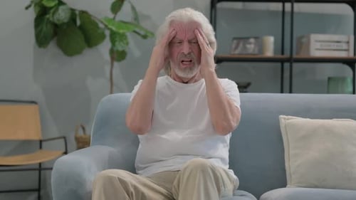 Senior Man With Headache Sits on Couch in Home