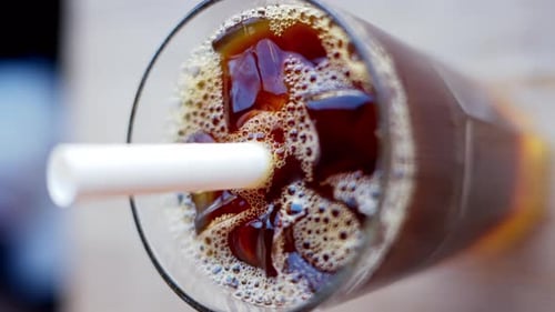 Cold brew coffee and bubble tea in a glass with ice and big white straw close up slow motion, vertic