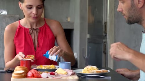 Woman Eats While Man Prepares Food in Kitchen