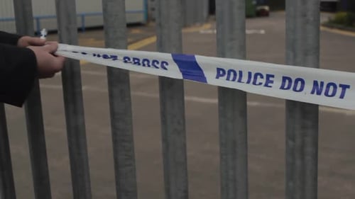 Close up as police detective cordons off an industrical unit by pacing police tape across the entran