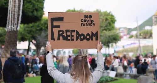 Woman protests coronavirus measures with crowd holding banner in the city