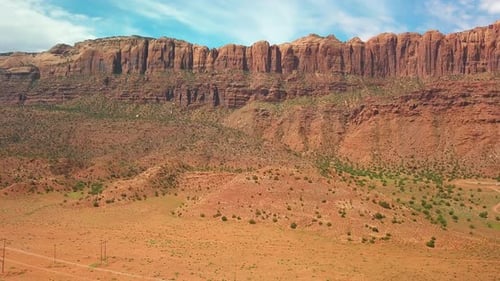 Drone shot of a steep red rock cliff towering over a desert valley. 4K
