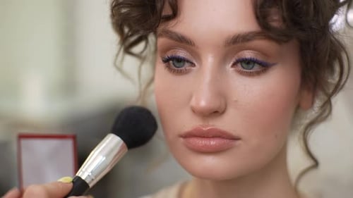 Nahaufnahme Gesicht einer wunderschönen jungen Frau, die vom Maskenbildner gegeben wird, trägt Puder und Rouge mit