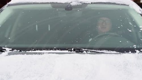 Junger Mann reinigt am Wintertag im Freien Schnee von der Autowindschutzscheibe