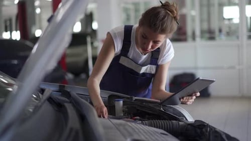 Female Mechanic Inspecting Car Components Under the Hood Woman in Overalls Checks the Engine and
